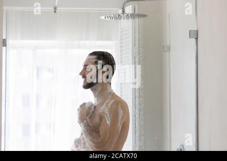 Jeune homme souriant prenant la douche du matin, debout dans la salle de bains moderne Banque D'Images