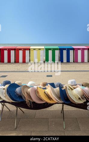 Chapeaux de paille à vendre devant des cabines de plage multicolores à Dunkerque, France. Banque D'Images