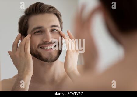 Gros plan miroir réflexion homme souriant touchant la peau sous les yeux Banque D'Images
