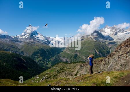 Jeune garçon observant un oiseau de proie à travers des jumelles avec des montagnes suisses comme toile de fond. Banque D'Images