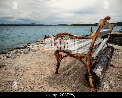 Vide banc en bois et rouillé sur le rivage de la mer en journée calme et nuageux. Banque D'Images