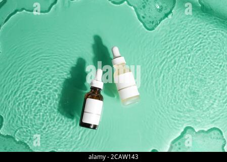 Ensemble cosmétique avec deux bouteilles de lotion naturelle maison ou d'huile essentielle sur un fond turquoise avec de l'eau sous la texture du verre, copier l'espace a Banque D'Images