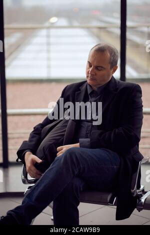 Gare. Homme mature dans les vêtements d'affaires est de dormir, assis dans la salle d'attente et d'attente pour le train. La soirée est sombre. Banque D'Images