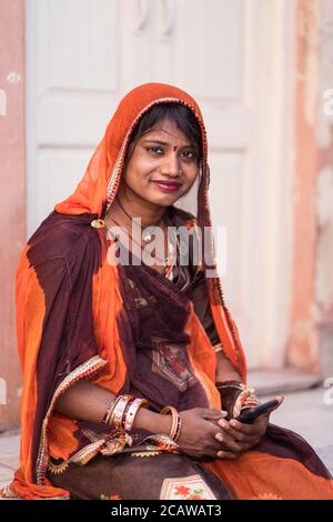 Jodhpur / Inde - 18 mars 2020: Portrait de la belle jeune femme Rajasthani avec des bijoux sur son visage et des vêtements traditionnels assis à l'aide du téléphone Banque D'Images