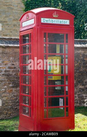 Téléphone britannique traditionnel dans le village converti en défibrillateur Banque D'Images