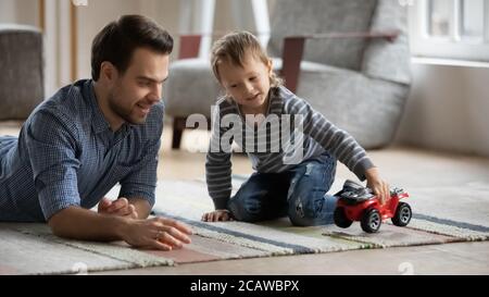 Un jeune père souriant joue avec un petit garçon dans une voiture-jouet préférée. Banque D'Images