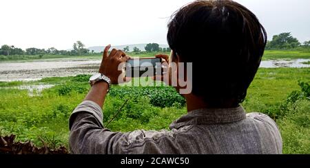 District Katni, Madhya Pradesh, Inde - 20 août 2019: Un homme de ville asiatique en cliquant sur l'image de smartphone dans un environnement naturel magnifique. Banque D'Images