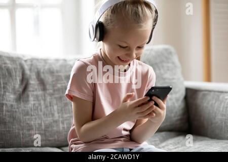 Petite fille blonde adorable regardant la vidéo drôle sur smartphone. Banque D'Images