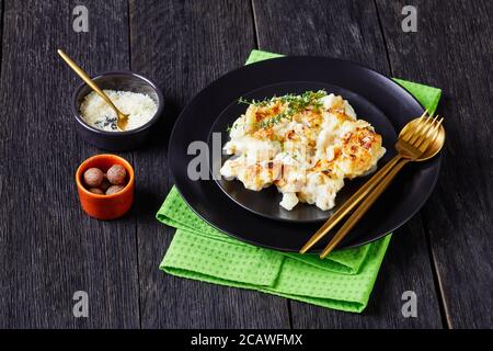 Cocotte de chou-fleur servie sur une assiette noire avec thym frais sur fond de bois avec muscade, parmesan râpé et couverts, Banque D'Images