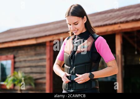 Bonne jeune femme surfeuse attacher la ceinture de sécurité veste contre maison Banque D'Images