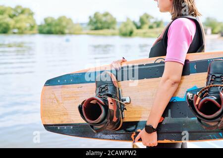 Jeune surfeur actif dans les vêtements de sport tenant la planche de surf tout en restant debout côté eau Banque D'Images