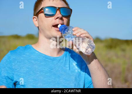 un sportif avec des lunettes boit de l'eau dans une bouteille pendant jogging et sports le matin Banque D'Images