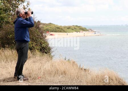 Un homme âgé regarde à travers des jumelles à Lepe Beach, Hampshire, Angleterre, Royaume-Uni, août 2020 Banque D'Images