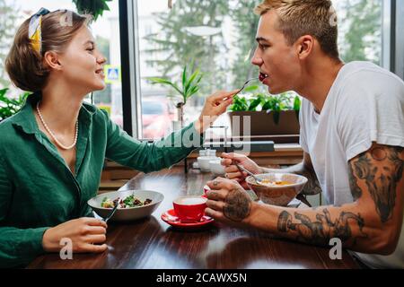 Homme avec une femme à la date dans un café, elle lui donne un morceau de son repas. Banque D'Images