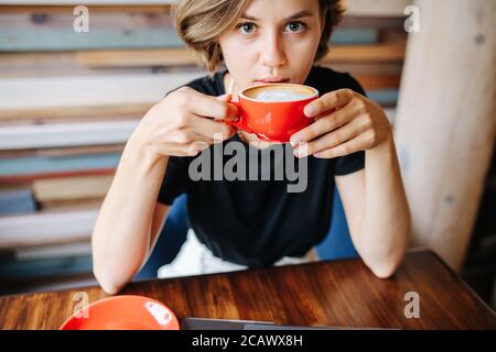 Une jeune femme attentionnés qui boit du café dans un café tout en regardant un appareil photo. Banque D'Images