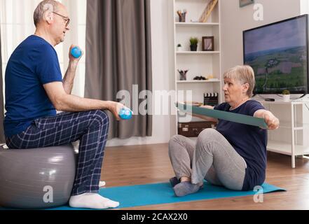 Des personnes âgées qui font de la forme physique ensemble à la maison en utilisant des haltères, du ballon suisse et un élastique. Personne âgée vie saine exercice à la maison, entraînement et entraînement, activité sportive à la maison sur tapis de yoga. Banque D'Images