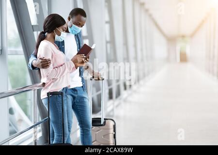 Vol en attente. Couple africain en masques médicaux debout au terminal avec des valises Banque D'Images