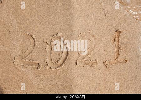 Une inscription avec les numéros de la future nouvelle année 2021 écrite sur le sable beige humide sur le bord de mer, un jour ensoleillé à côté de la vague dans le séjour Banque D'Images
