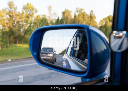 Novosibirsk, Russie - 06.26.2020: Vue arrière dans le rétroviseur latéral d'une berline bleue avec le reflet d'un dépassement sur une route asphaltée sur un Banque D'Images