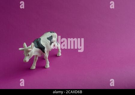 Figurine de vache blanche avec taches noires sur fond violet. Produits agricoles, concept de l'élevage. Copier l'espace. Vue de dessus en angle. Mise au point sélective. Banque D'Images