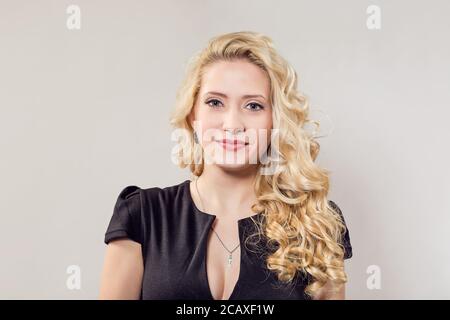 Femme blonde moderne en noir tenue et les accessoires smiling at camera sur fond gris Banque D'Images