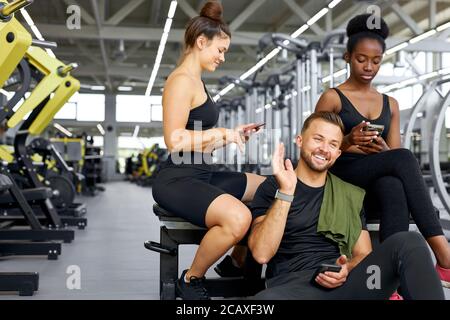 jeunes sportifs parlant en salle de gym, après l'entraînement, les femmes de race mixte et l'homme caucasien se reposant appréciant la conversation terminé l'entraînement Banque D'Images