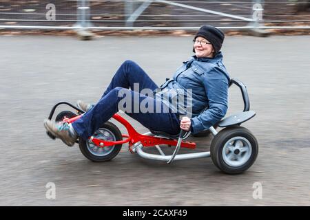 Femme d'âge moyen souriante qui profite d'une balade sur un kart en tricycle allongé, Londres, Royaume-Uni Banque D'Images