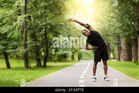 Sportif africain flexible s'étendant dans un parc public Banque D'Images