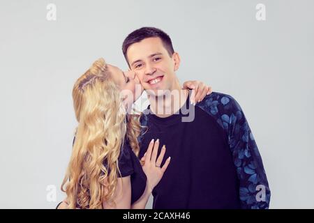 Blonde woman kissing beau jeune homme dans la joue debout sur fond gris Banque D'Images