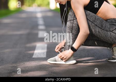 Fille sportive nouant des lacets de chaussures avant de courir, se préparer pour le jogging en plein air Banque D'Images