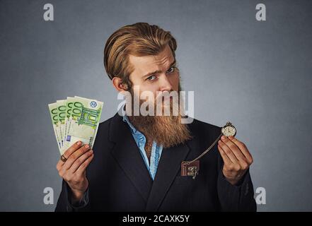 Le temps est argent concept. Handsome businessman hipster barbu homme sceptique sérieux en chemise bleue avec trésorerie devises et rétro montre de poche isolé sur Banque D'Images