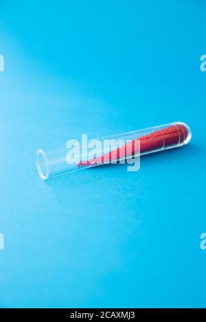 Tube à essai transparent avec granules rouges sur fond bleu. Banque D'Images