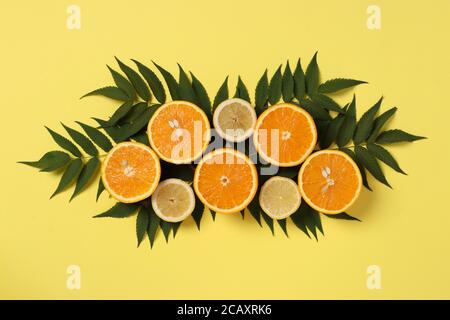 Composition de moitiés de citrons et d'oranges avec feuilles vertes sur fond jaune vif, Flat Lay, vue de dessus Banque D'Images