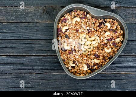 Granola à la noix de cajou dans un plat à pâtisserie en forme de cœur. Table en bois noir Banque D'Images