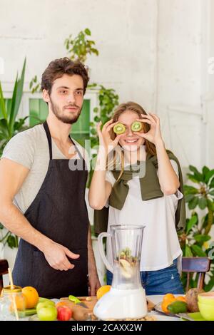 fille positive avec kiwi sur ses yeux et homme beau debout dans la cuisine. amusement, divertissement Banque D'Images