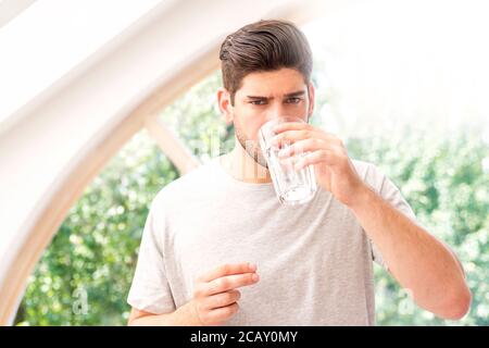 Beau homme tenant un verre d'eau dans sa main tout en prenant la pilule. Banque D'Images