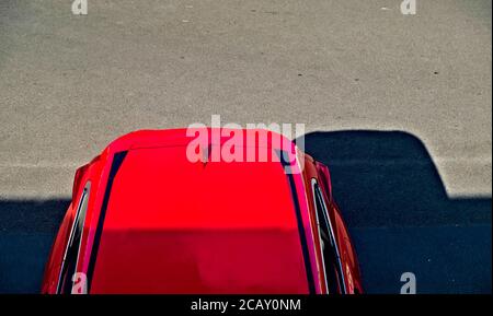 Voiture SUV moderne rouge garée dans un parking en asplalt noir, vue de dessus de la section arrière, soleil et zones d'ombre. Banque D'Images