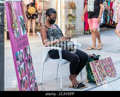 Punta Umbria, Huelva, Espagne - 7 août 2020: Une femme africaine immigrée côté rue salon de coiffure. Ici, le coiffeur attend de créer des tresses en h. Banque D'Images