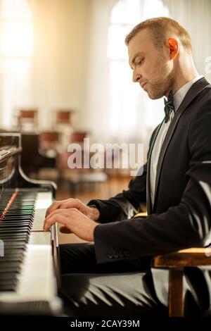 jeune homme caucasien élégant en costume élégant et formel, joue avec élégance au piano. un pianiste professionnel joue de la musique classique Banque D'Images