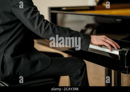 court non reconnaissable homme en costume jouant du piano sur une scène. beau gars avec élégance jouer du piano, s'entraîner avant la performance Banque D'Images