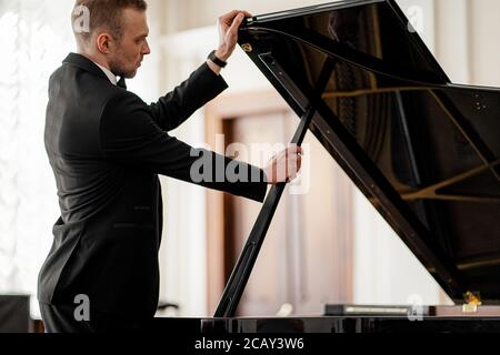 jeune caucasien en costume formel ouvrant le piano avant de jouer dessus, pianiste professionnel va s'entraîner à jouer du piano Banque D'Images