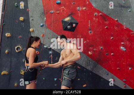 belle fille belle attrayante avec un instructeur dans la salle de gym d'escalade. gros plan photo. copier l'espace. homme aidant la fille à porter l'équipement. Banque D'Images