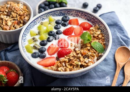 Yaourt avec granola, bleuets, fraises et tranches de kiwi dans un bol. Vue en gros plan. Bol de céréales pour petit déjeuner sain avec beaucoup de fruits. Nettoyer e Banque D'Images