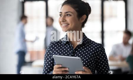 Une femme d'affaires indienne rêveuse et souriante tenant une tablette Banque D'Images