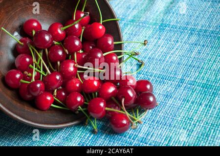 Cerises mûres et juteuses aux queues vertes dans un plat en céramique sombre. Fond de baies, composition avec cerises Banque D'Images