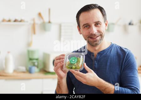 Portrait d'un homme à barbe mûr tenant une boîte à salade et souriant à l'appareil photo tout en appréciant le service de livraison de nourriture, l'espace de copie Banque D'Images