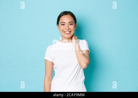 Portrait de belle modeste fille asiatique souriante regardant heureux à l'appareil photo, grinning et touchant cou timide, se précipitant sur compliment, se tenant satisfait Banque D'Images