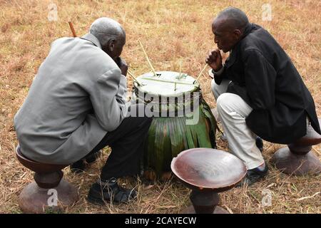 Deux vieux rwandais boivent dans un grand pot lors d'un festival traditionnel « Umuganura » et un siège traditionnel rwandais vacant dans le district de Nyagatare, au Rwanda Banque D'Images