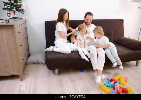 portrait de famille caucasienne amicale s'asseoir détente profitez de passer du temps ensemble à la maison en utilisant une tablette, portant des vêtements blancs décontractés Banque D'Images