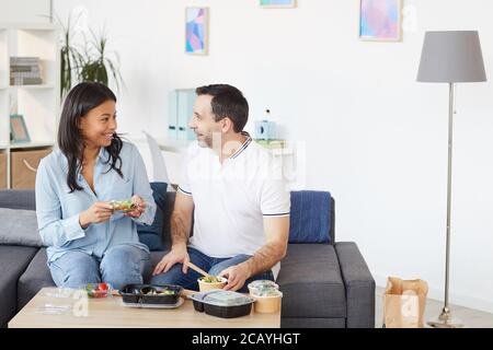 Portrait d'un homme et d'une femme souriants bavardant avec joie tout en dégustant un déjeuner à emporter au bureau ou à la maison, dans un espace de travail Banque D'Images